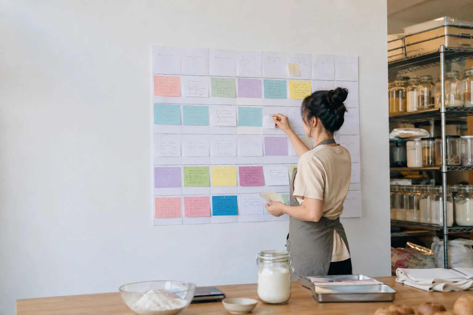 A baker plans a month of production using color cards beside ingredients and a working prep table.